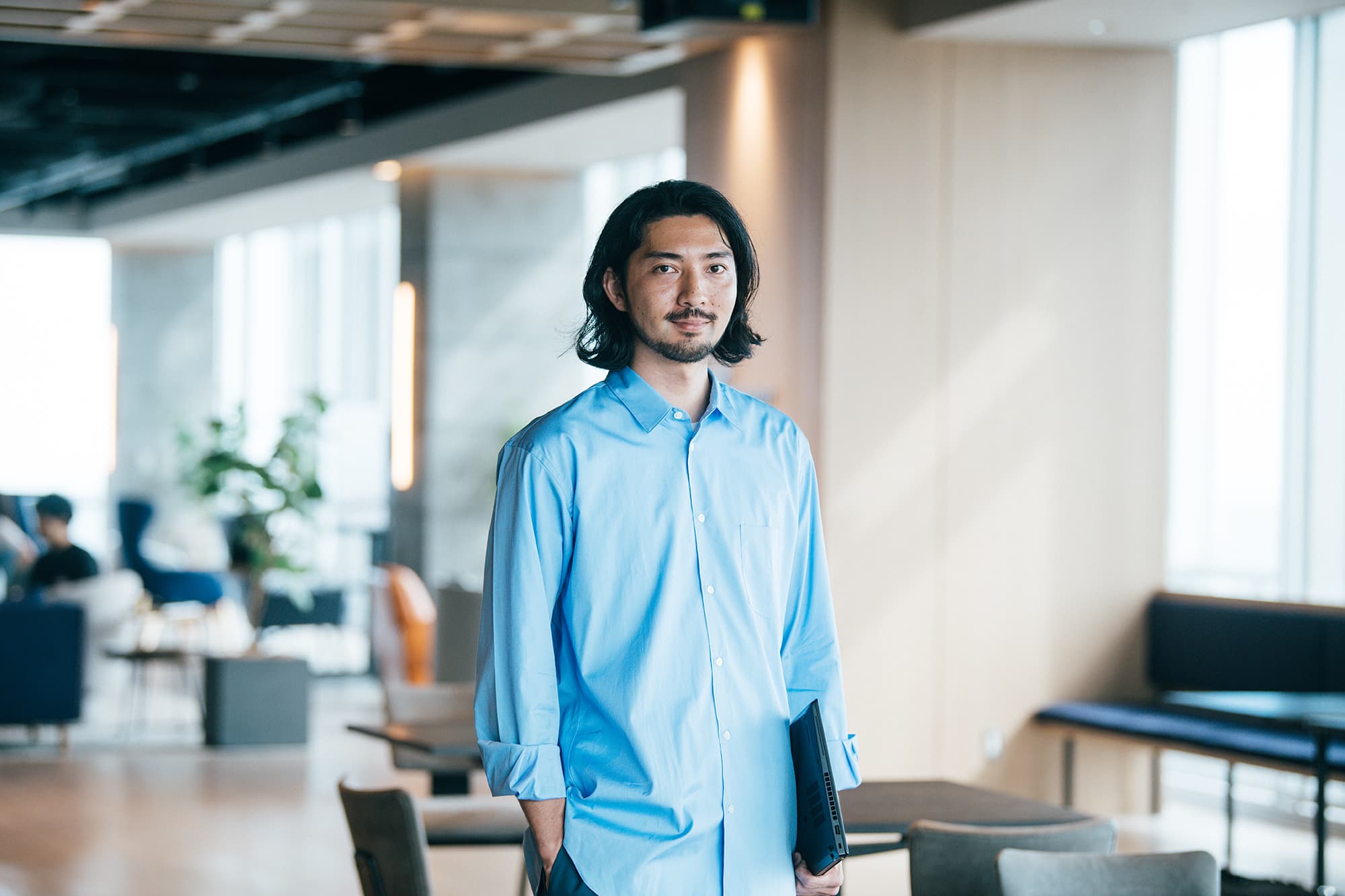 リクルートでデザインディレクターを務める小島清樹が、オフィスでPCを片手にキャリアについて話す様子